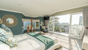 A bedroom with a large bed, a view of the outdoors, and a balcony.