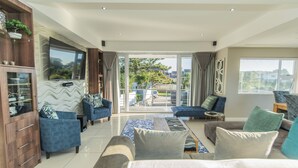 A modern living room with a large TV, blue sofas, a coffee table, and a view of the outdoors.