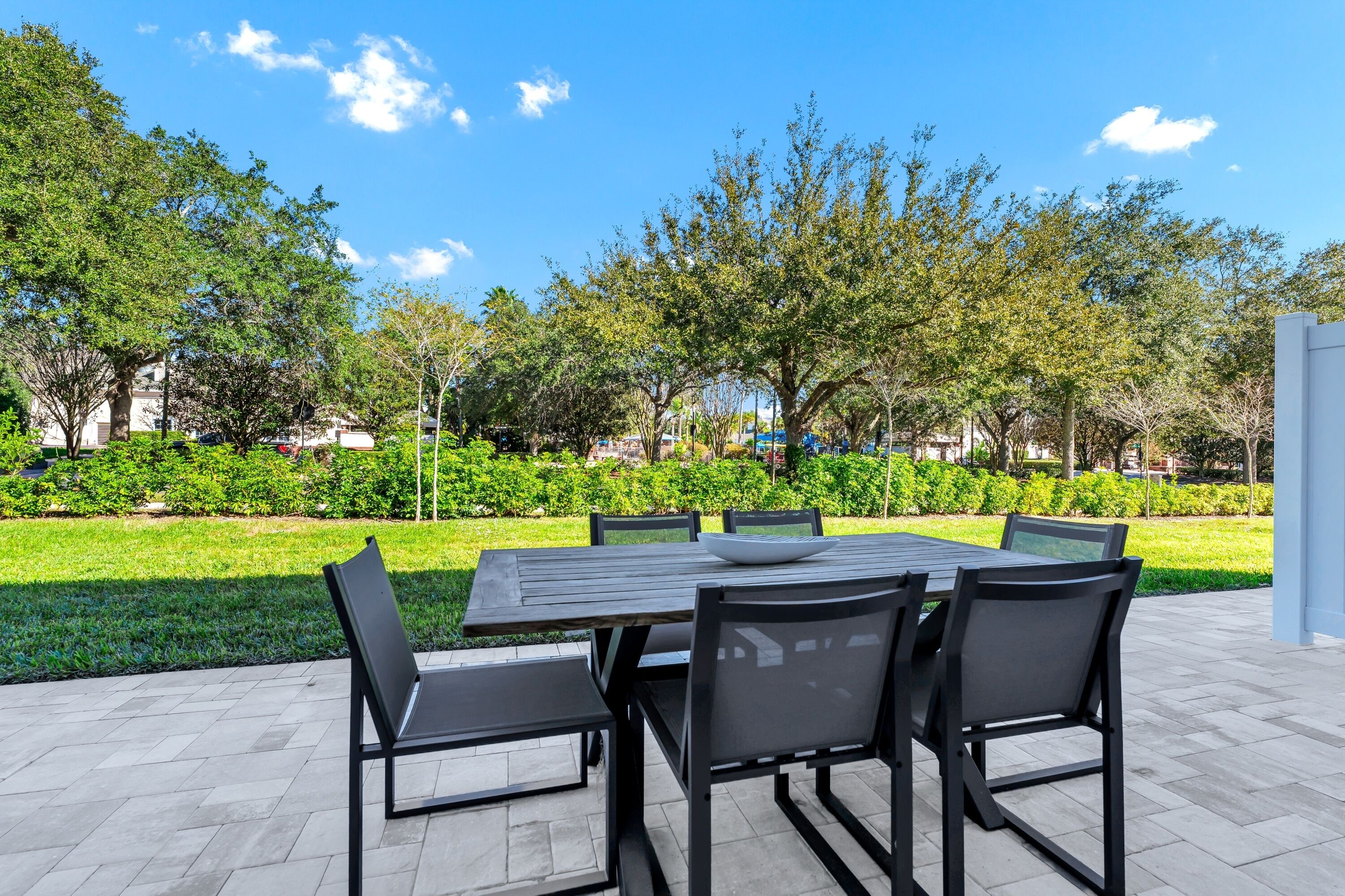An outdoor patio with a rectangular table and four chairs, surrounded by a well-maintained lawn and trees.