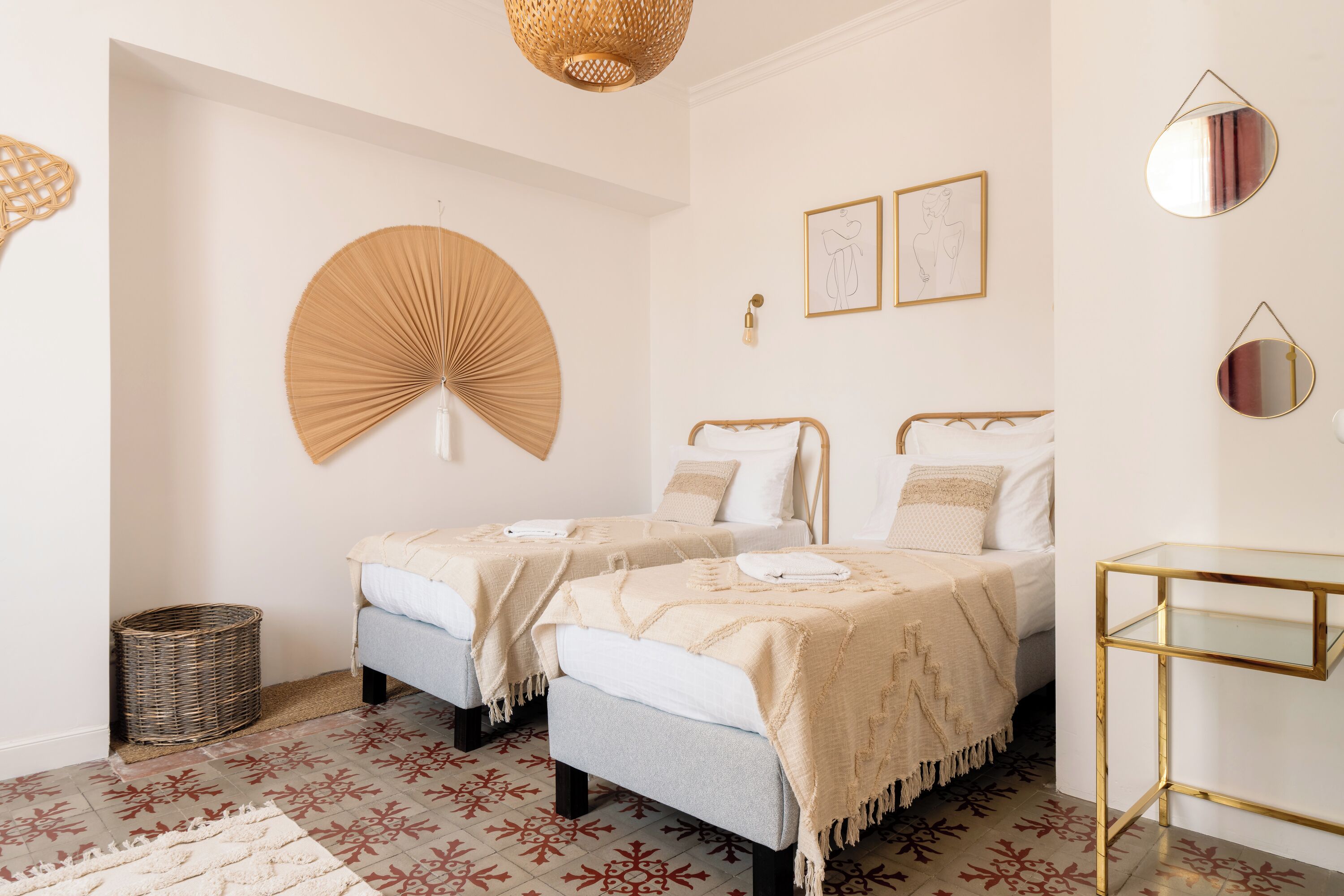 Ein Schlafzimmer mit zwei Betten, einem Korbwäscheschrank, einem kleinen Tisch und einem Wandventilator.