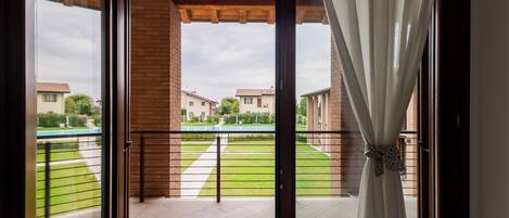 Un balcón con vista a una zona residencial, suelo de baldosas y una cortina.