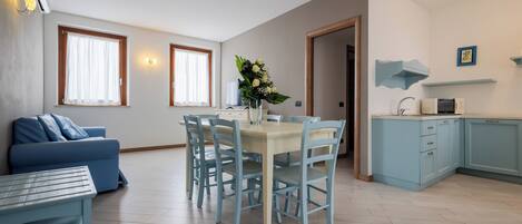 A modern living room with a blue sofa, a dining table with chairs, and a kitchen area with light blue cabinets.