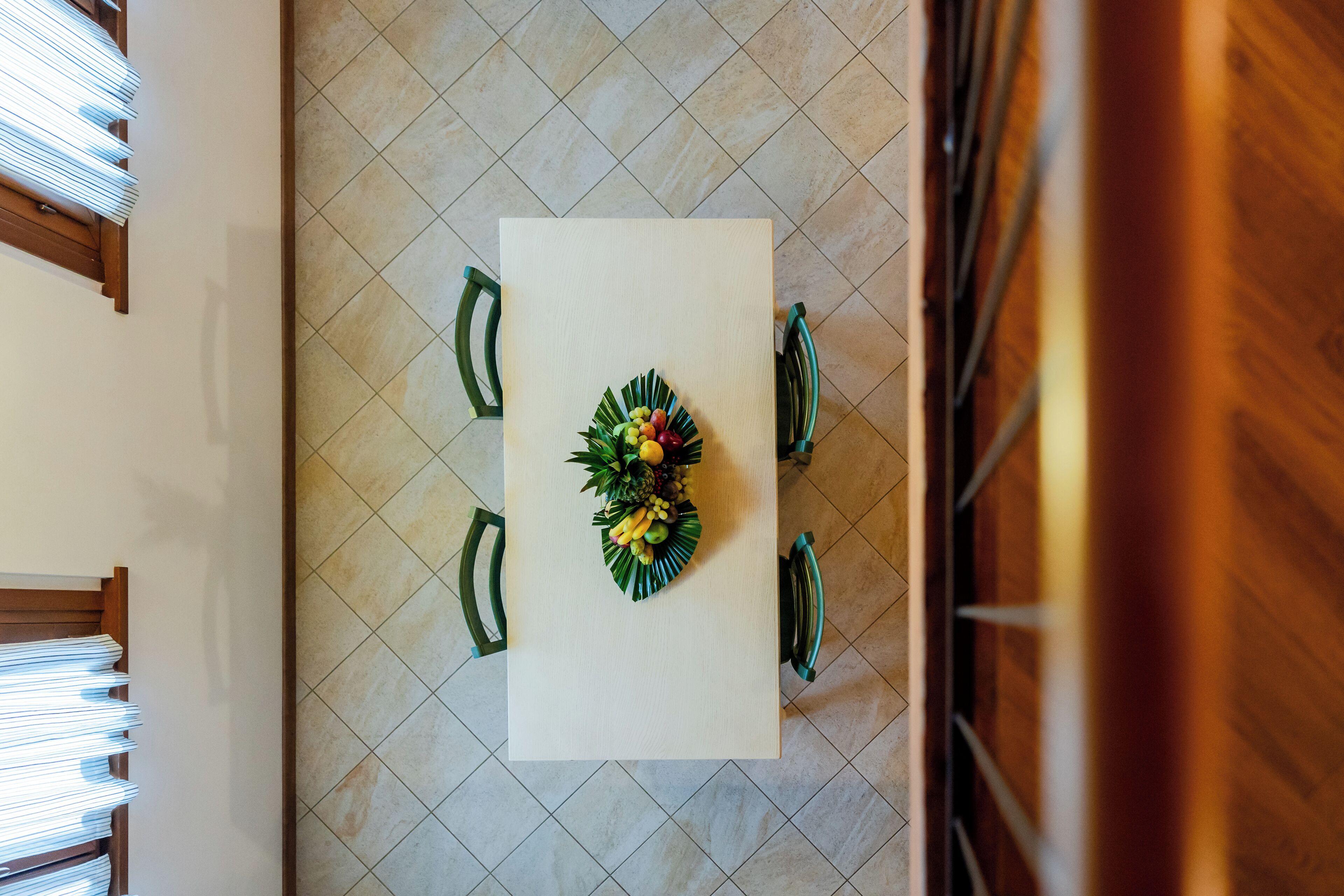 A dining table with a floral centerpiece, surrounded by chairs, in a room with tiled flooring and wooden walls.