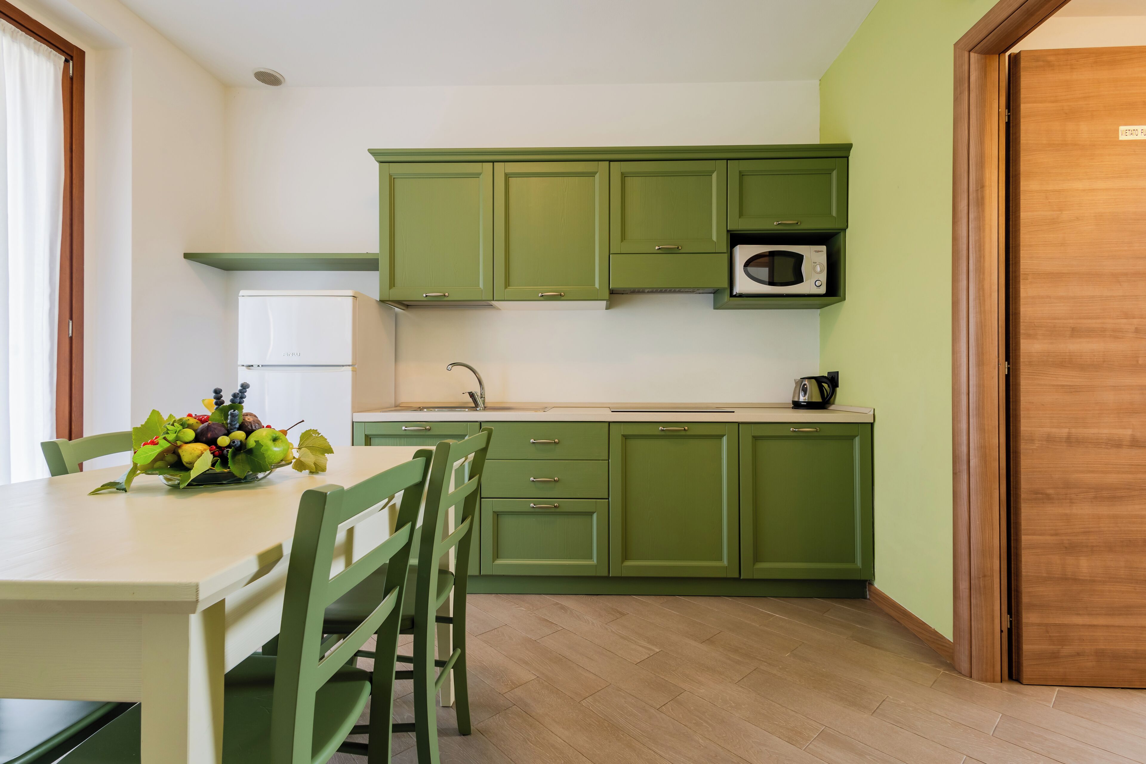 Une cuisine avec des meubles de rangement verts, un four à micro-ondes et un panier de fruits posé sur le plan de travail.