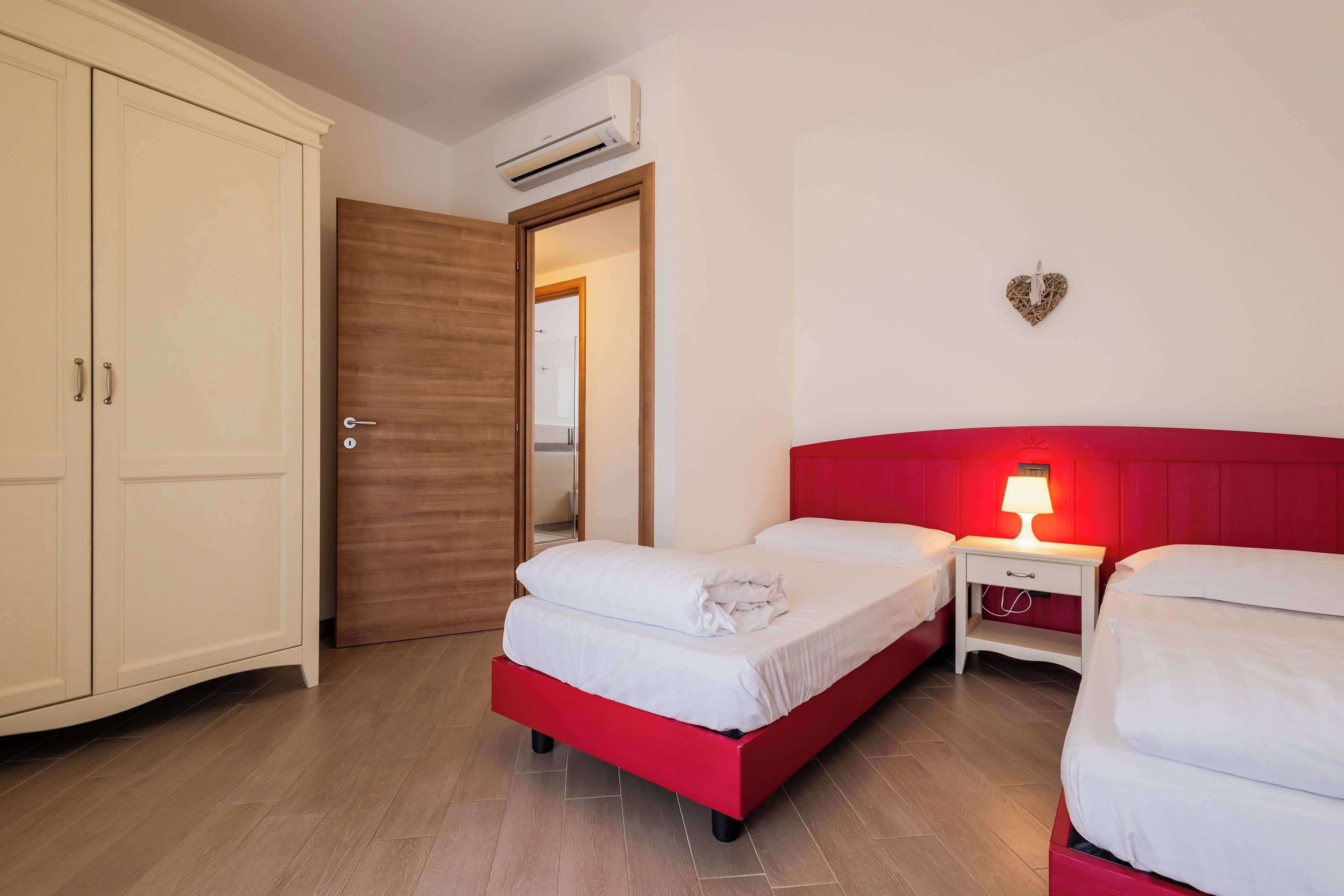 Un dormitorio con dos camas, un armario y una mesita de noche con lámpara.