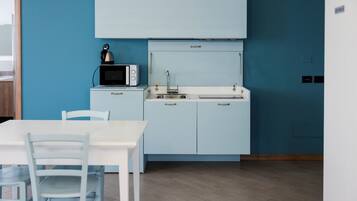 Cuina compacta amb microones, rentapelats i armaris, situada davant d'una paret color turquesa.