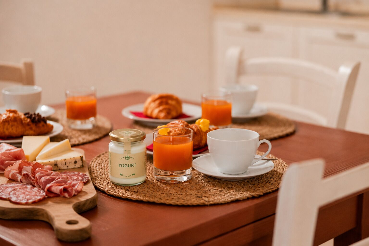En morgenmadsopstilling med et træbord, et glas yoghurt, croissanter, ost, lufttørret kød og glas med appelsinjuice.