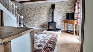 Una habitación con escalera de madera, chimenea con estufa negra, televisor sobre una mesa de madera y alfombra estampada en el suelo.