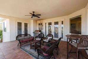 A covered patio area with wicker furniture, a ceiling fan, and a barbecue grill.