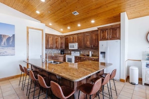 A kitchen with wooden cabinets, a central island with stools, a microwave, and a refrigerator. - Las Palmas Resort #808 | All-Inclusive Amenities (Saint George)