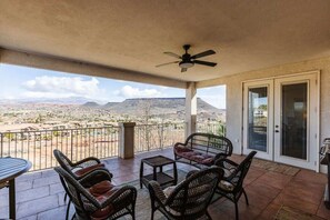 A covered patio with wicker furniture, a ceiling fan, and a view of a desert landscape. - Las Palmas Resort #808 | All-Inclusive Amenities (Saint George)