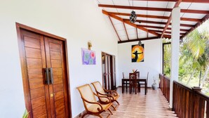 A covered porch with wooden chairs, a dining table, and a view of the outdoors. - Sunsei Beach Negombo (Negombo)