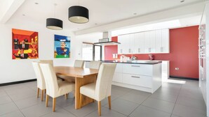 A modern kitchen with white cabinets, a wooden dining table, and two pendant lights. - Bellevue (Newtownabbey)
