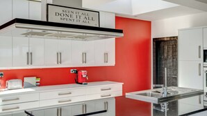 A modern kitchen with white cabinets, a red accent wall, and a stainless steel sink. - Bellevue (Newtownabbey)