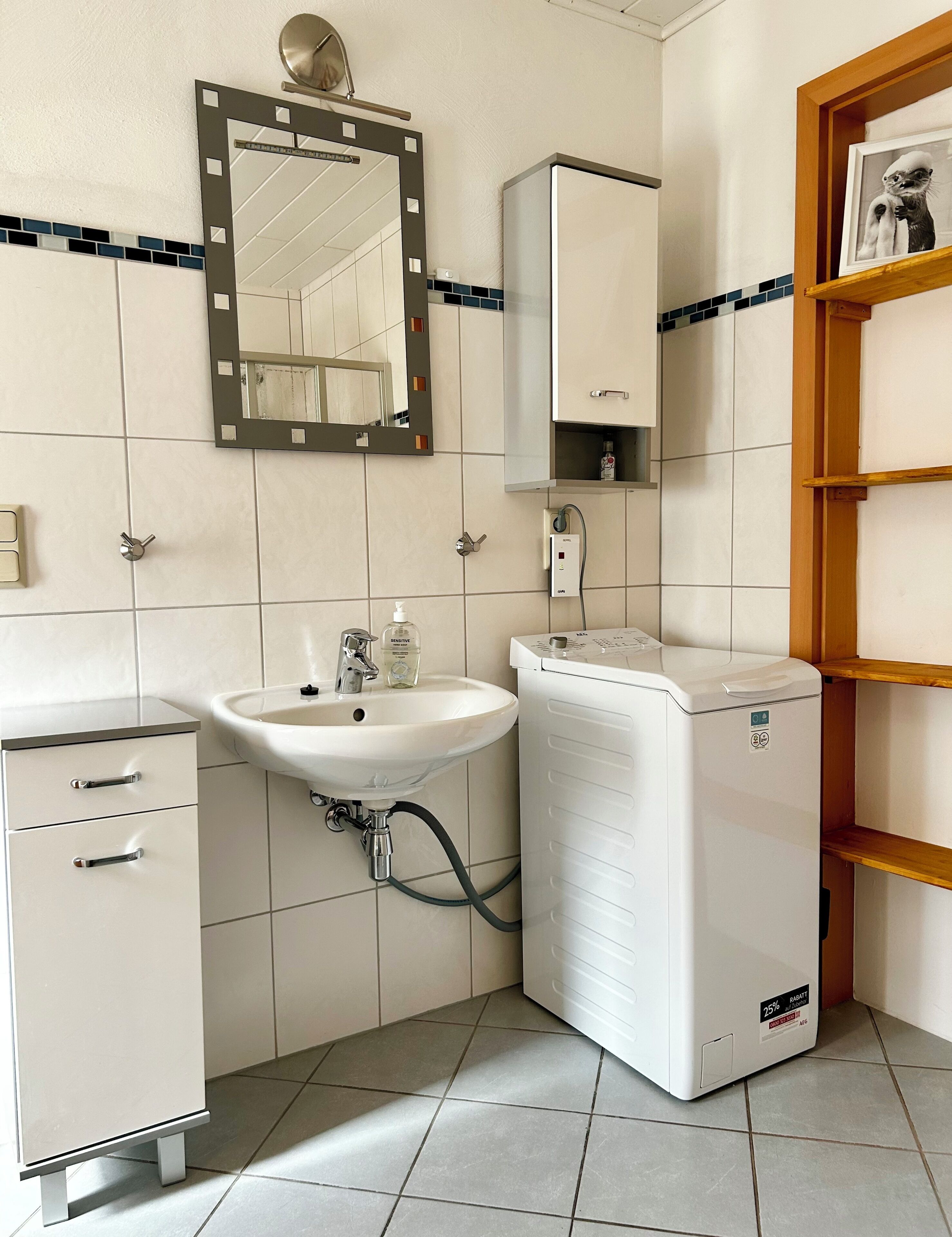 Ein Badezimmer mit Waschbecken, Spiegel, Schrank und einer weißen Waschmaschine.