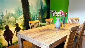 Uma mesa de jantar com cadeiras de madeira, um vaso com flores e um mural com uma paisagem florestal.