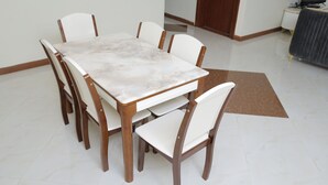 Een eettafel met zes stoelen, een witte vloer en een bruin vloerkleed.
