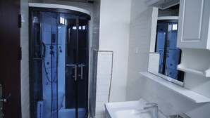 Een moderne badkamer met een douchecabine van glas, een witte wastafel en een spiegel erboven.