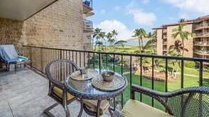 Ein Balkon mit Korbmöbeln, einem Glastisch und Blick auf einen Golfplatz und den Ozean.