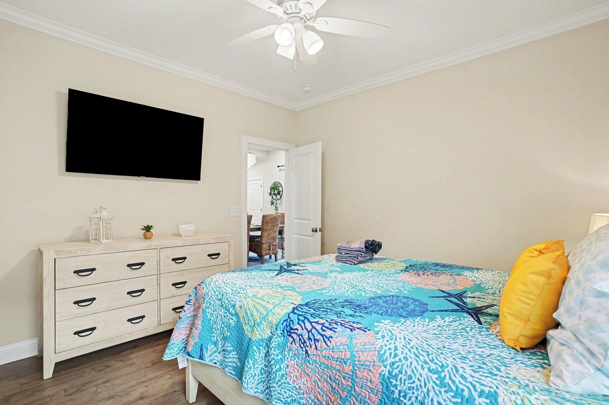 Een slaapkamer met een bed, een dressoir, een televisie aan de muur en een plafondventilator.