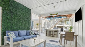 A modern living area with a blue sofa, a wooden coffee table, a green wall, and a bar area with a staircase. - Brand NEW Heatable PRIVATE Pool| Mini-Golf |Hot Tub| Steps2Beach| Ground Floor Suite, Perfect for Families, Close to Everything in NMB! (North Myrtle Beach)