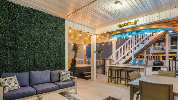 A modern interior with a sofa, coffee table, and a bar area with a staircase. - Brand NEW Heatable PRIVATE Pool| Mini-Golf |Hot Tub| Steps2Beach| Ground Floor Suite, Perfect for Families, Close to Everything in NMB! (North Myrtle Beach)