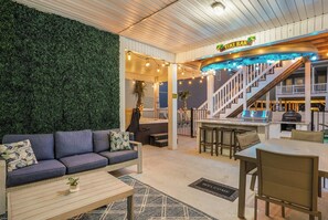 A modern interior with a sofa, coffee table, and a bar area with a staircase. - Brand NEW Heatable PRIVATE Pool| Mini-Golf |Hot Tub| Steps2Beach| Ground Floor Suite, Perfect for Families, Close to Everything in NMB! (North Myrtle Beach)