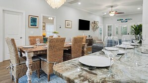A dining area with a marble table, wicker chairs, and a chandelier. - Brand NEW Heatable PRIVATE Pool| Mini-Golf |Hot Tub| Steps2Beach| Ground Floor Suite, Perfect for Families, Close to Everything in NMB! (North Myrtle Beach)