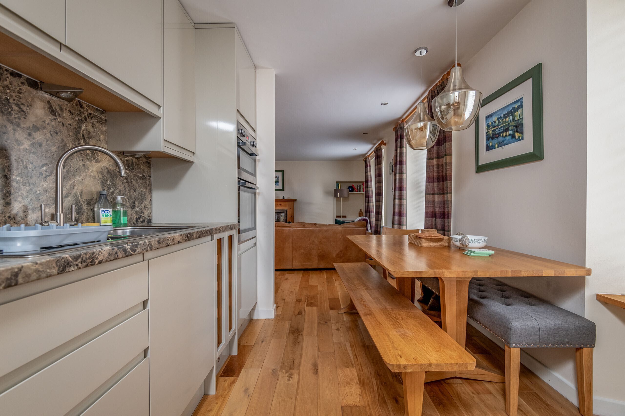 A modern kitchen with a marble backsplash, wooden flooring, and a dining area with a bench.