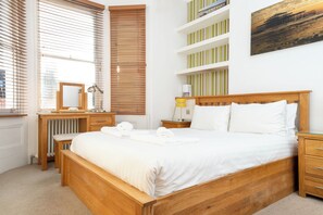 A neatly arranged bedroom with a wooden bed, a bedside table, a desk with a chair, a radiator, and a shelf with books. - Modern 1BDR Retreat | Near Queens Park & Seafront (Brighton and Hove)