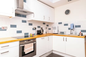 A modern kitchen with white cabinets, a stainless steel oven, a coffee maker, and a clock on the wall. - Modern 1BDR Retreat | Near Queens Park & Seafront (Brighton and Hove)
