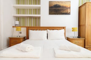A hotel room with a bed, two bedside tables, a wooden wardrobe, a striped wall, and a sunset view. - Modern 1BDR Retreat | Near Queens Park & Seafront (Brighton and Hove)