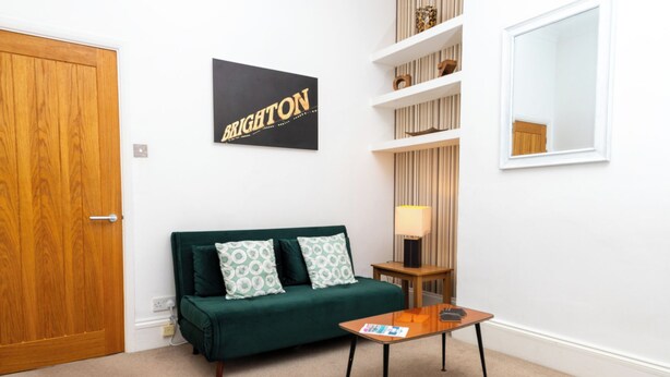 Una habitación con un sofá verde, una pequeña mesa de madera, una lámpara y un letrero en la pared que dice 'BRIGHTON'.