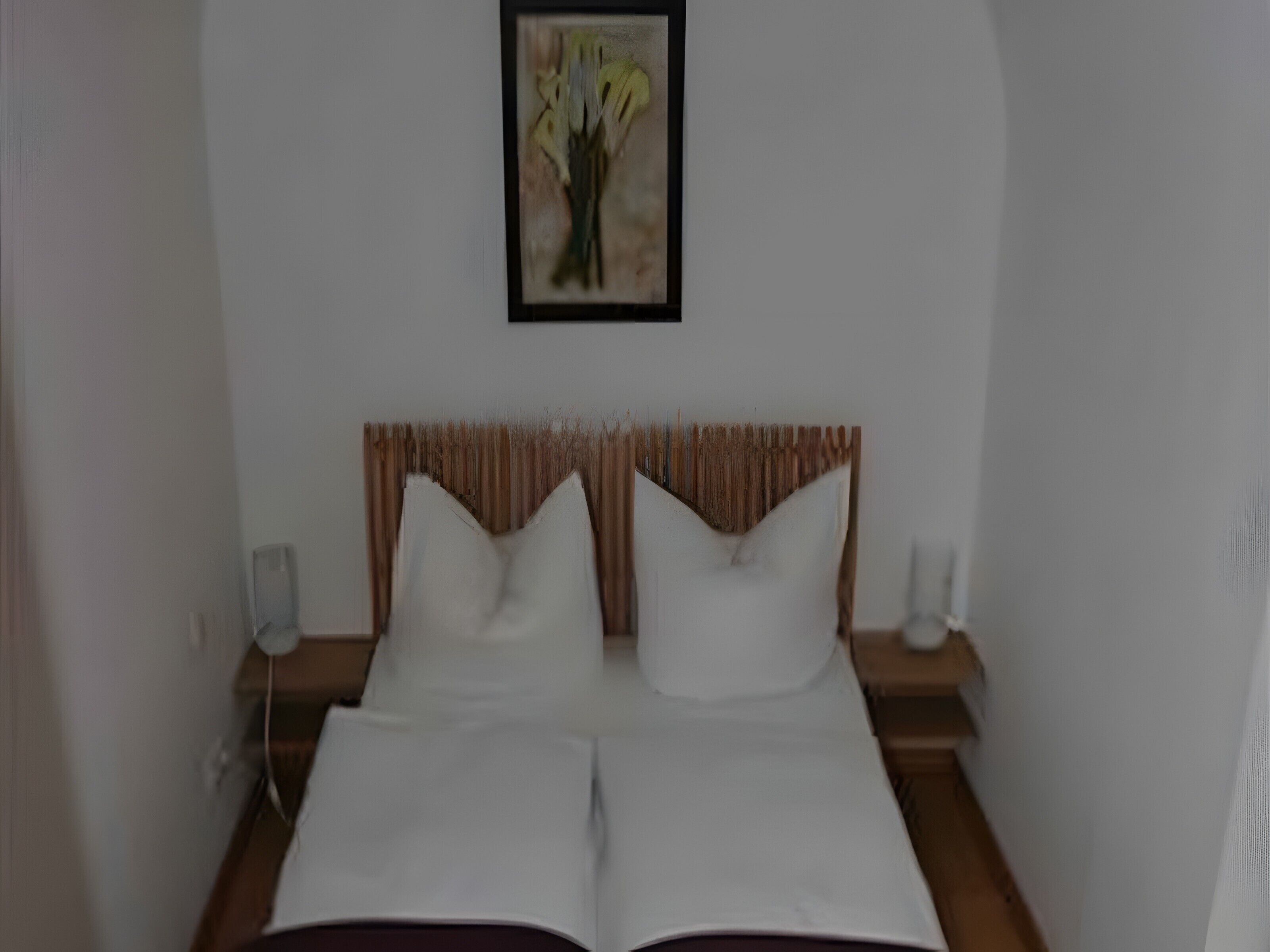 A neatly made bed with white linens, a wooden headboard, and a framed artwork above it.