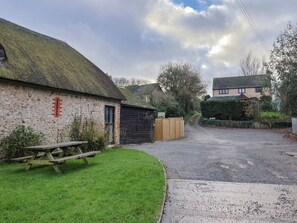 A rural road leading to a stone building with a thatched roof, a wooden fence, and a picnic table. - Apple Cottage (Bridport)