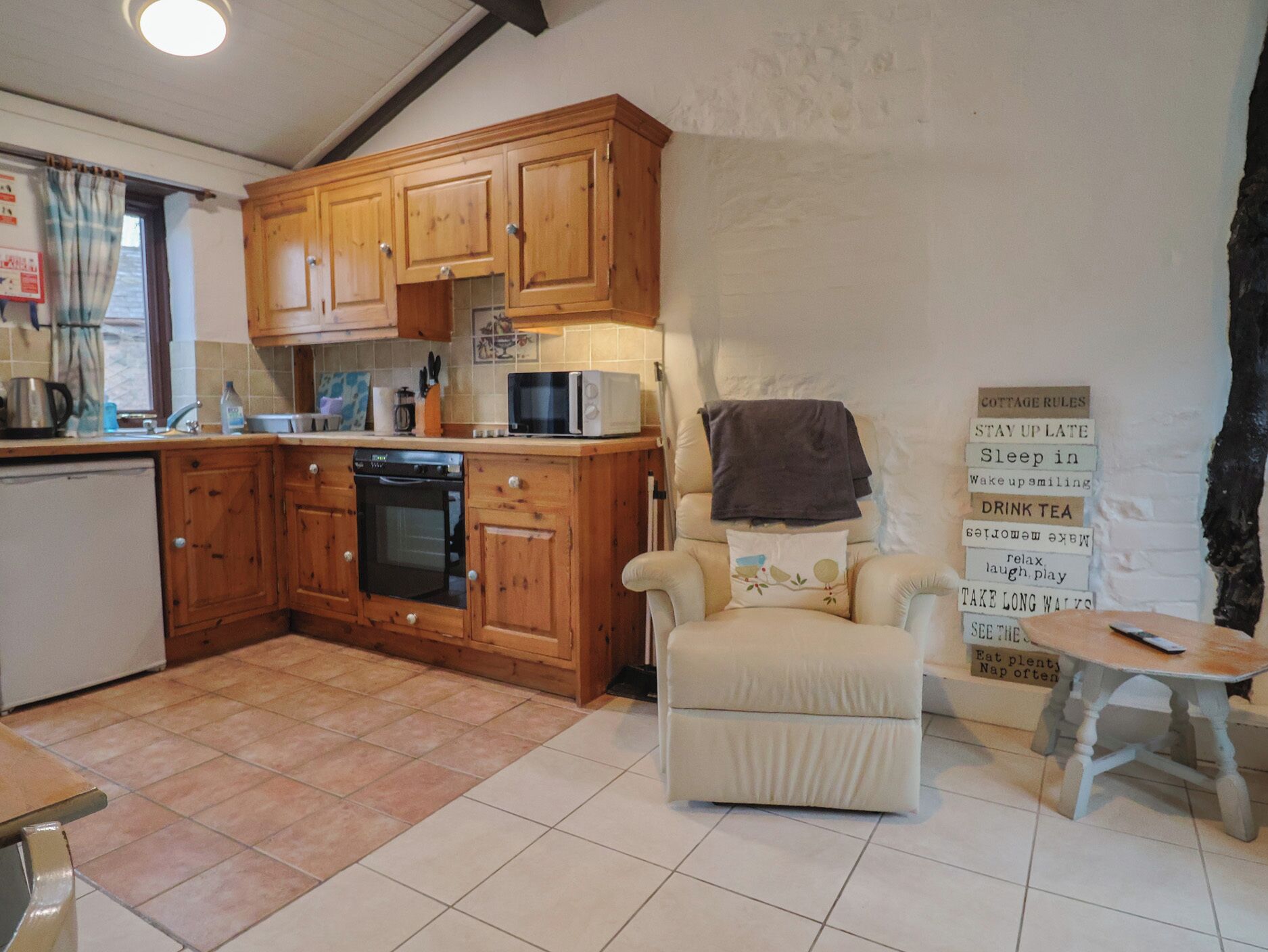 A kitchen with wooden cabinets, a microwave, and a small dining area with a chair and table.
