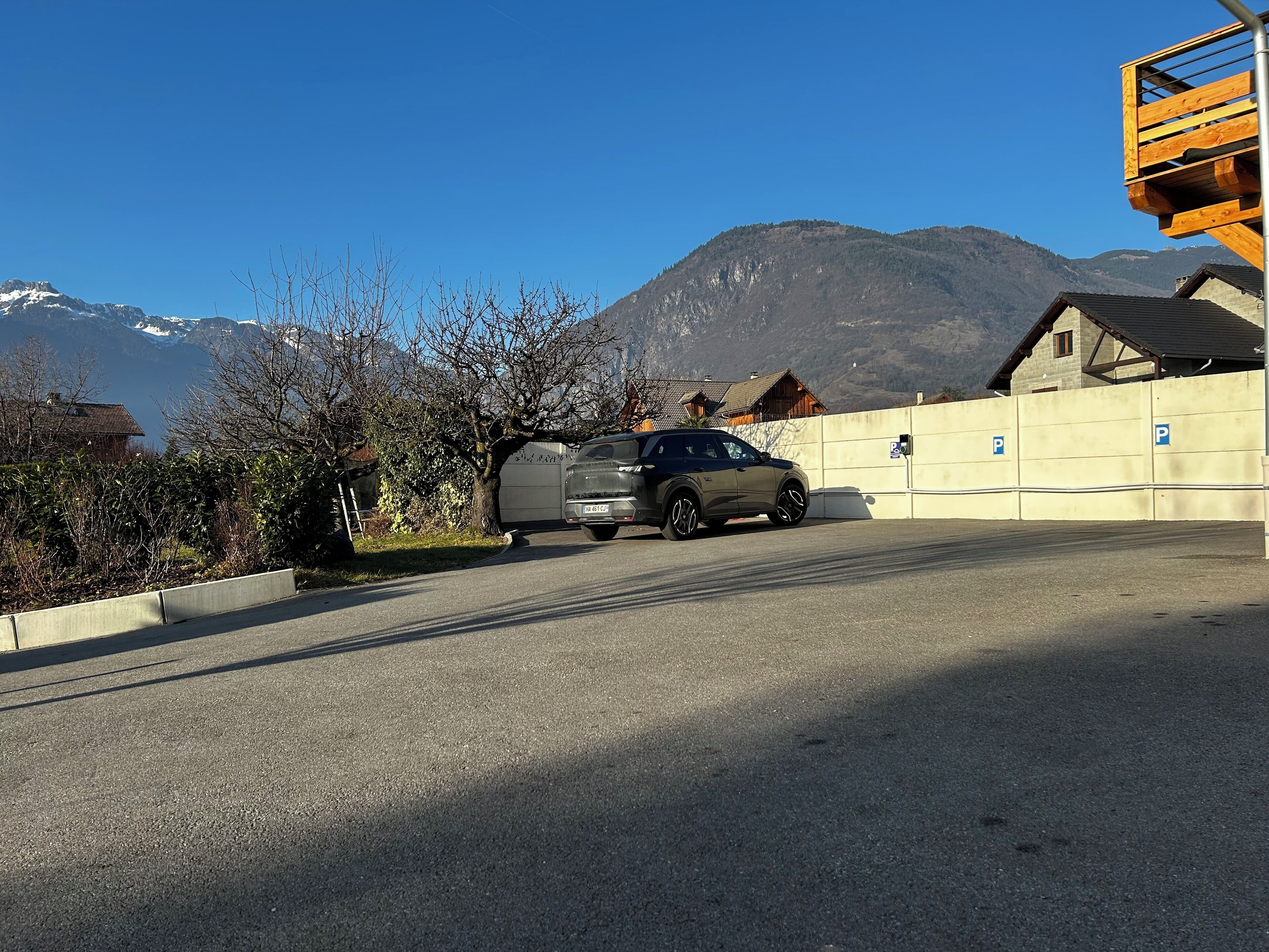 A parking area with a car and a trailer, surrounded by buildings and mountains in the background.