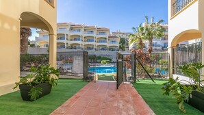 A courtyard with artificial grass, a swimming pool, and multi-story buildings in the background. - Vacation Apartment 'Golf Del Sur Oasis' with Shared Pool, Private Terrace & Wi-Fi (Santa Cruz de Tenerife)