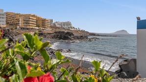 A coastal hotel with multiple floors, a rocky shoreline, and a clear view of the sea. - Vacation Apartment 'Golf Del Sur Oasis' with Shared Pool, Private Terrace & Wi-Fi (Santa Cruz de Tenerife)