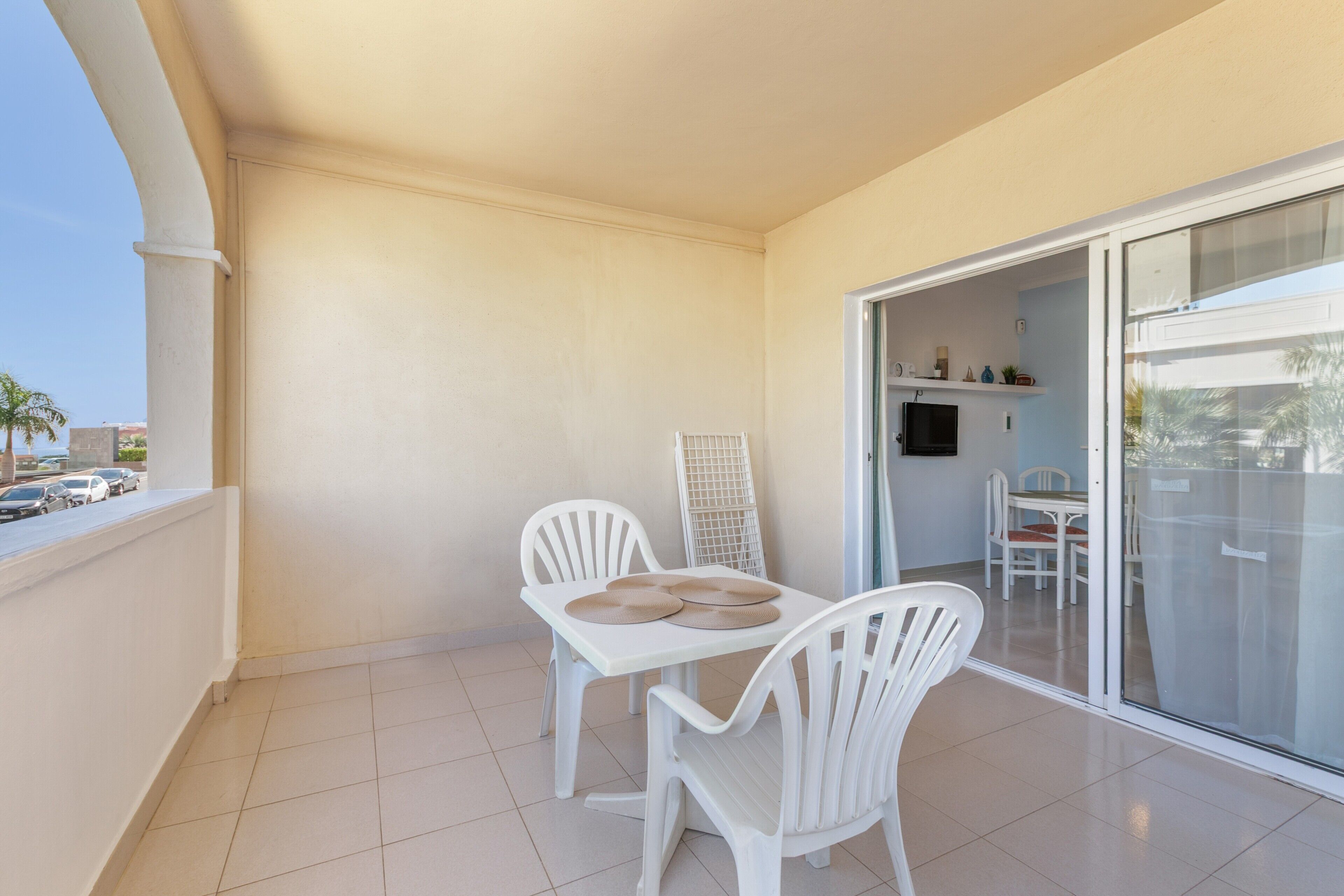 A balcony with a white table and chairs, a white radiator, and a glass door leading to an indoor area with a table and chairs.