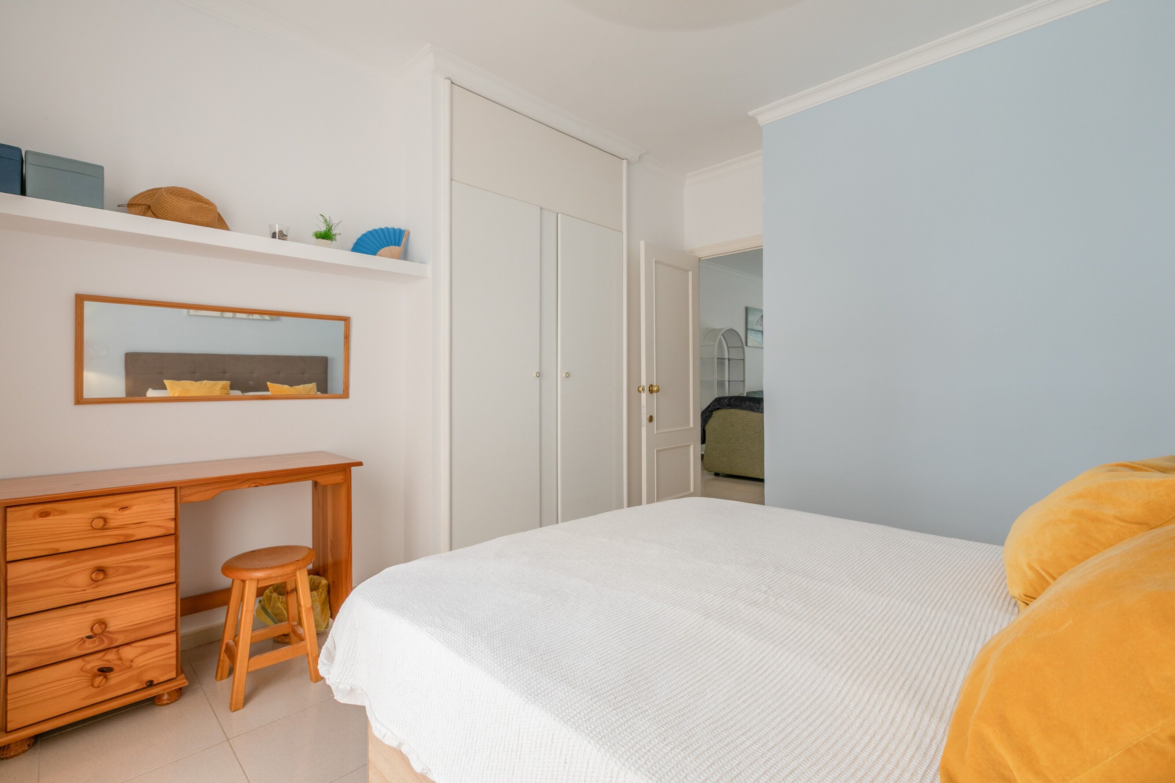 A bedroom with a bed, a wooden dresser, a mirror, and a wardrobe.