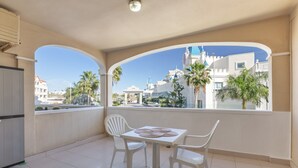 A balcony with a table and chairs, a view of a castle-like building, and palm trees. - Vacation Apartment 'Golf Del Sur Oasis' with Shared Pool, Private Terrace & Wi-Fi (Santa Cruz de Tenerife)