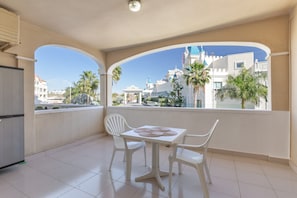 Un balcón con mesa y sillas, vista a un edificio parecido a un castillo y palmeras.