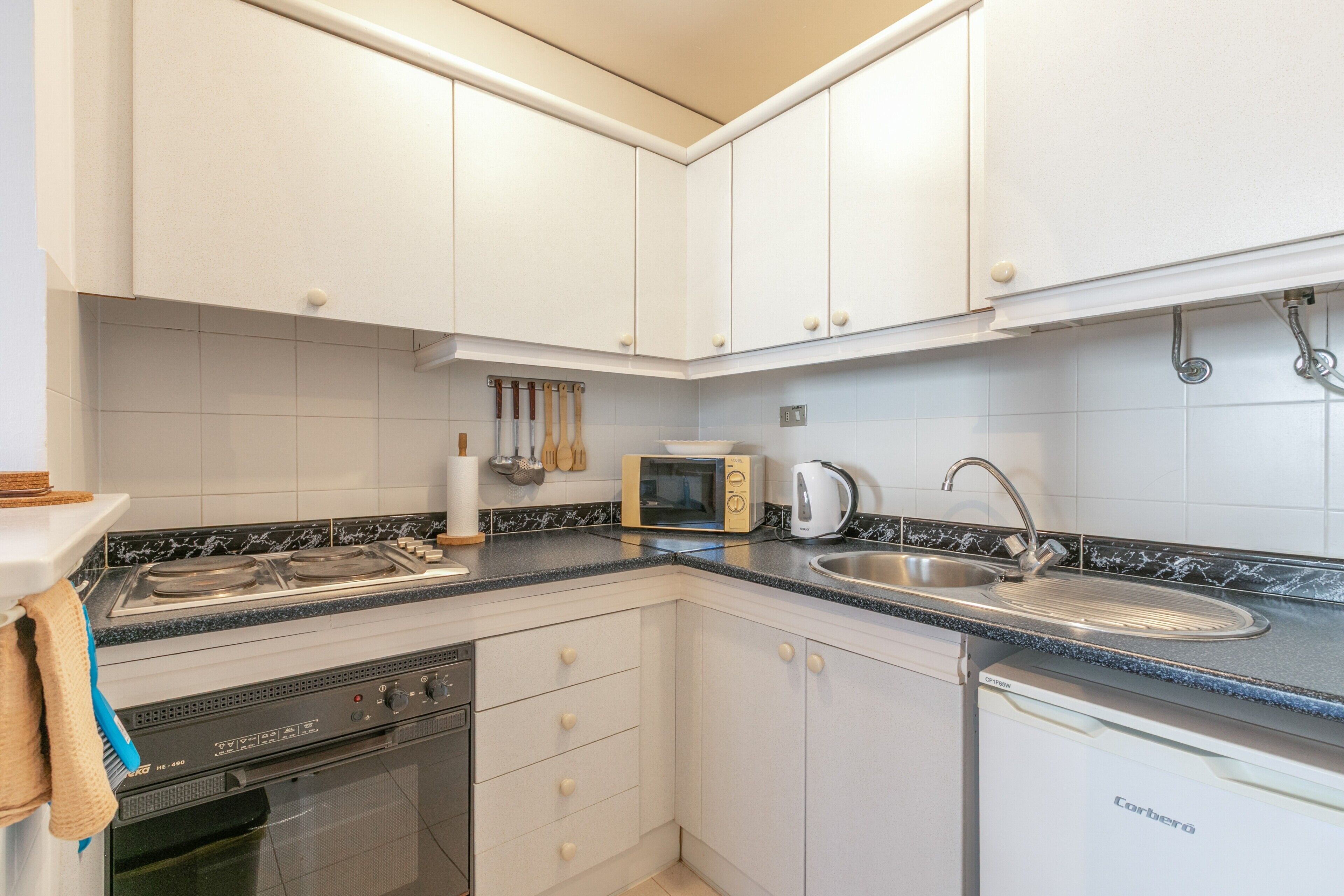 A kitchen with white cabinets, a microwave, a kettle, and a dishwasher.