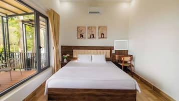 Habitació d'hotel amb llit, escriptori, cadira, finestra amb cortines i balcó.