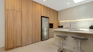 A modern kitchen with wooden cabinets, a stainless steel refrigerator, a marble countertop, and a bar area with stools. - Sea You in Batemans Bay - Steps from the Beach (Batemans Bay)