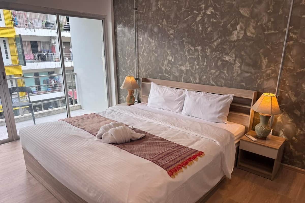 A modern hotel room with a large bed, two bedside tables, and a view of the city through large windows.