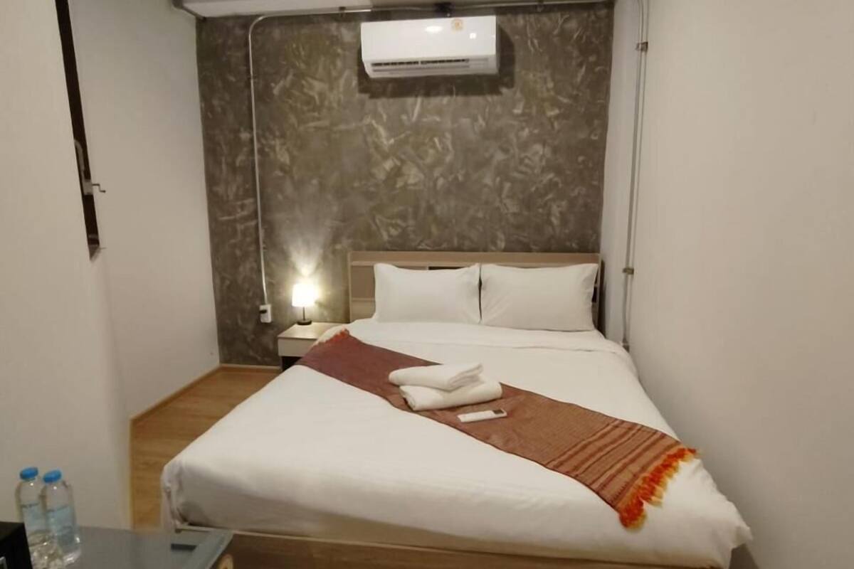 A compact hotel room with a bed, bedside table, and a small kitchenette.