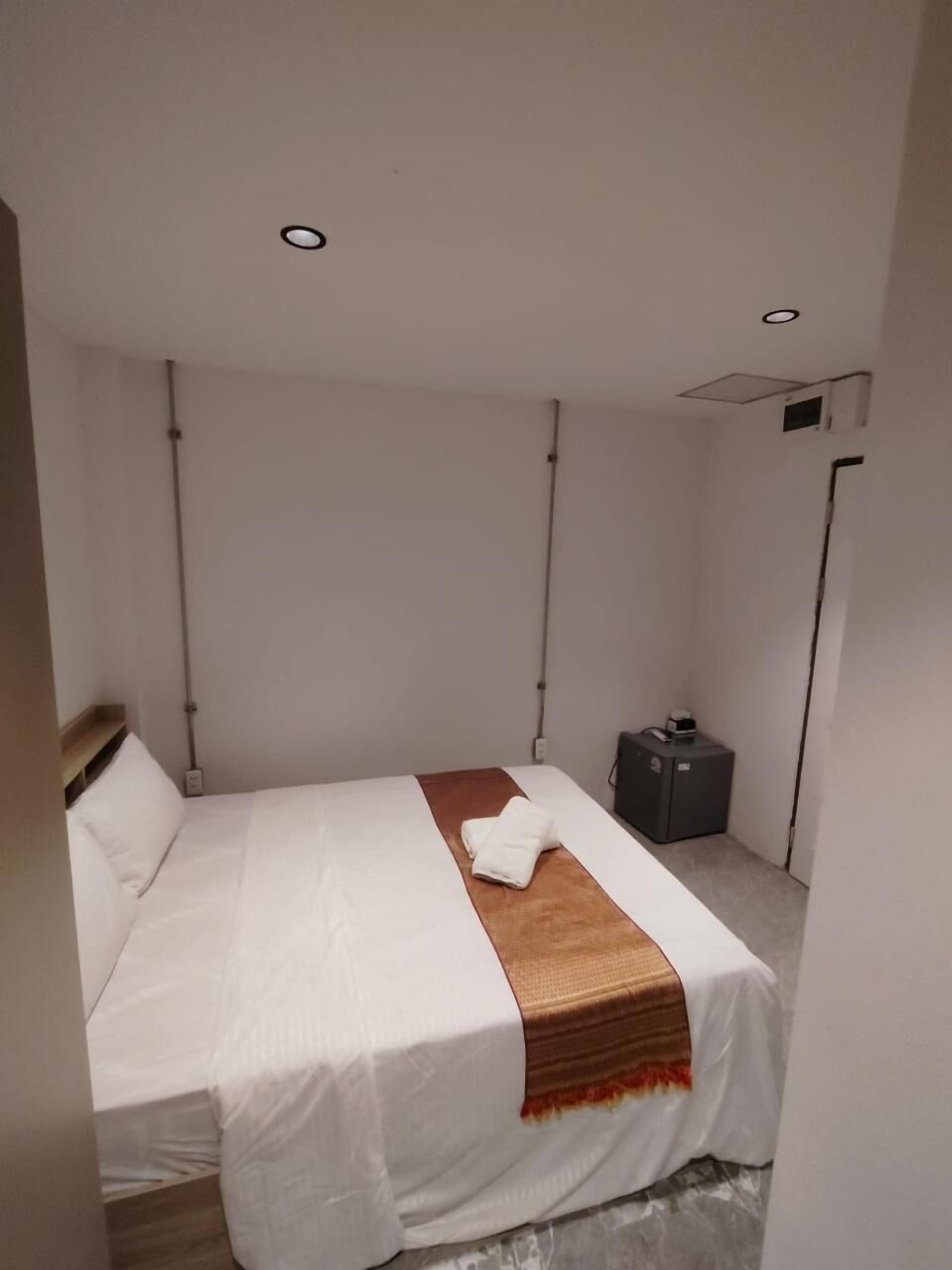 A modern hotel room with a neatly made bed, a small bedside table, and a suitcase.