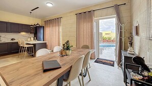 A modern kitchen with dark cabinets, a wooden dining table, and a view of the outdoors. - Peaceful Home with Private Pool and Rooftop Jacuzzi (Ix-Xagħra)